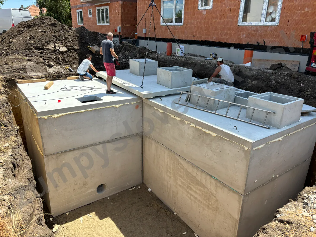 Montážny tím ukladá hydraulickou rukou kryciu dosku s dvoma komínmi na betónovú nádrž