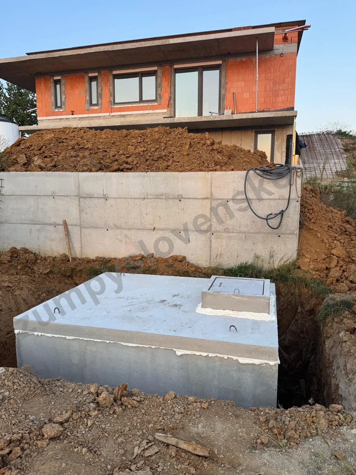 Betónová nádrž osadená pri rozostavanom dome s doskou, nízkym komínom a poklopom