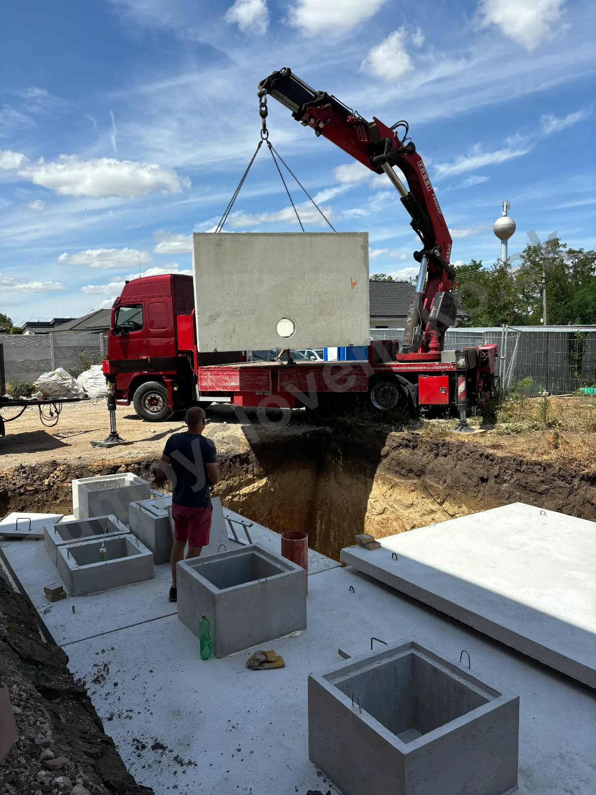 Hydraulická ruka červeného vozidla zdvíha betónový diel pri pripravenom výkope